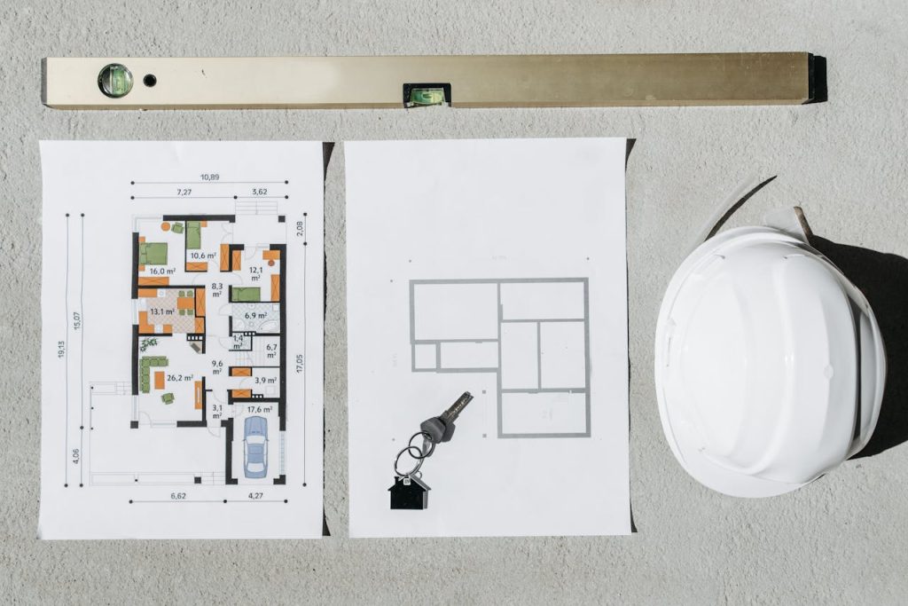 spirit-level-and-house-plans-in-overhead-view-7937315 Blueprints, spirit level, and hard hat symbolize house planning.